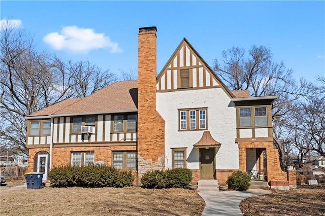 english style home featuring stucco siding, a chimney, roof with shingles, cooling unit, and brick siding