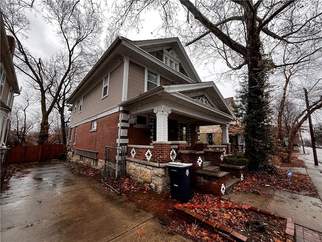 american foursquare style home with covered porch, brick siding, and fence