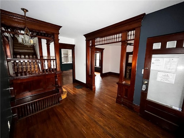 hallway featuring baseboards, stairway, wood finished floors, an inviting chandelier, and ornate columns