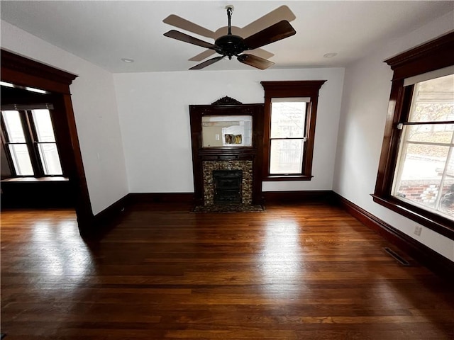 unfurnished living room featuring a stone fireplace, wood finished floors, visible vents, and baseboards