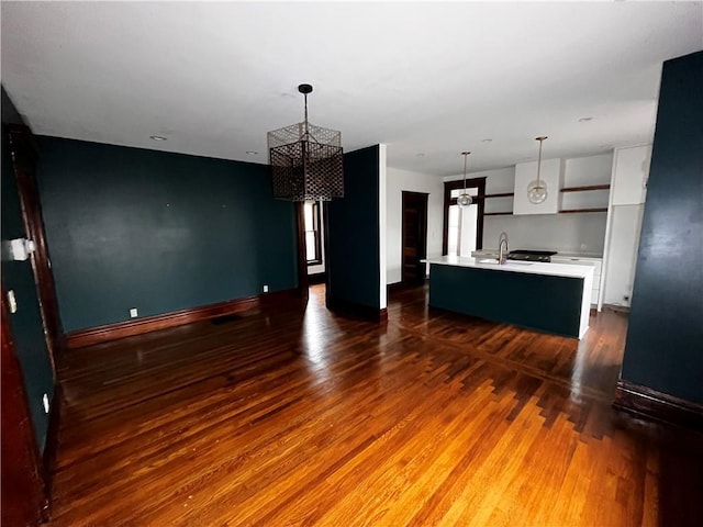 kitchen featuring a kitchen island with sink, wood finished floors, white cabinets, light countertops, and pendant lighting