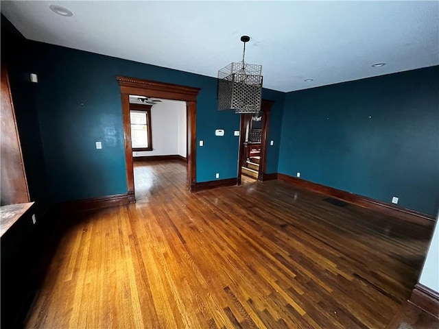 unfurnished dining area featuring a notable chandelier, baseboards, and wood finished floors