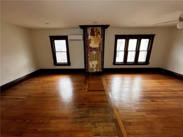 spare room featuring a wall unit AC, a ceiling fan, baseboards, and wood finished floors