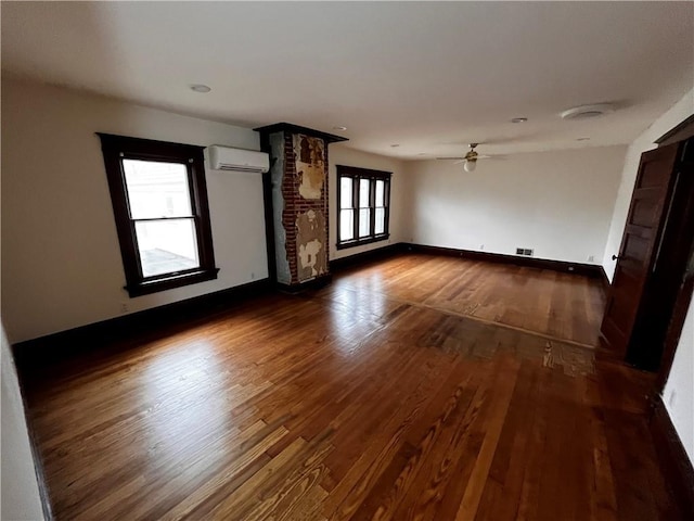 unfurnished room with ceiling fan, dark wood-style flooring, visible vents, baseboards, and a wall mounted air conditioner