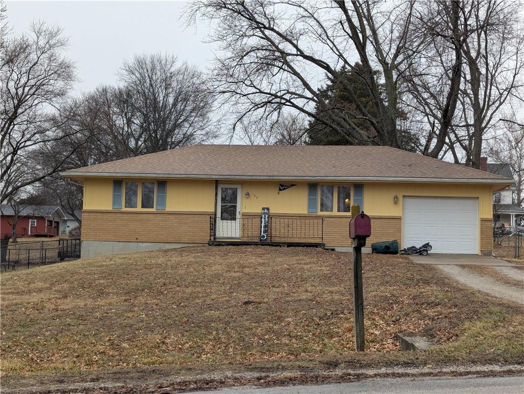 ranch-style house with brick siding, fence, covered porch, a garage, and driveway