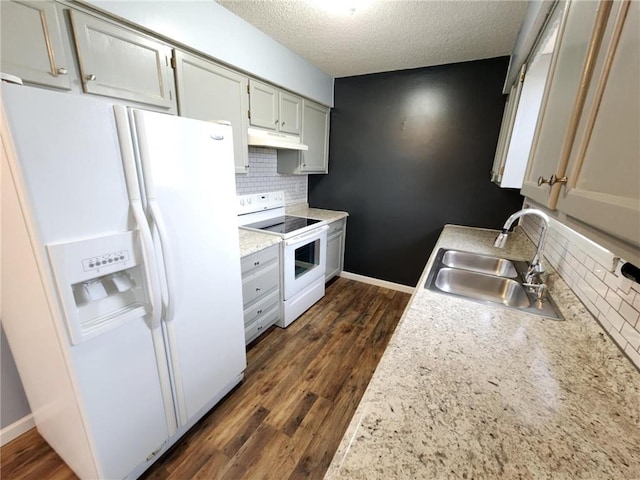 kitchen with white appliances, decorative backsplash, dark wood-style floors, under cabinet range hood, and a sink