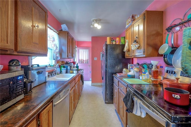 kitchen featuring baseboards, a sink, appliances with stainless steel finishes, dark countertops, and brown cabinets