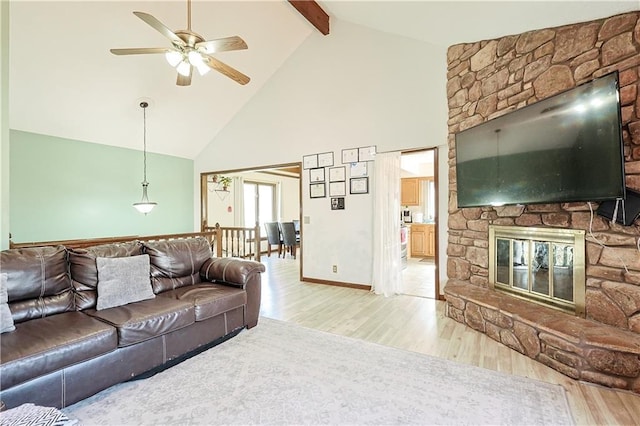 living room with ceiling fan, beamed ceiling, a fireplace, wood finished floors, and high vaulted ceiling