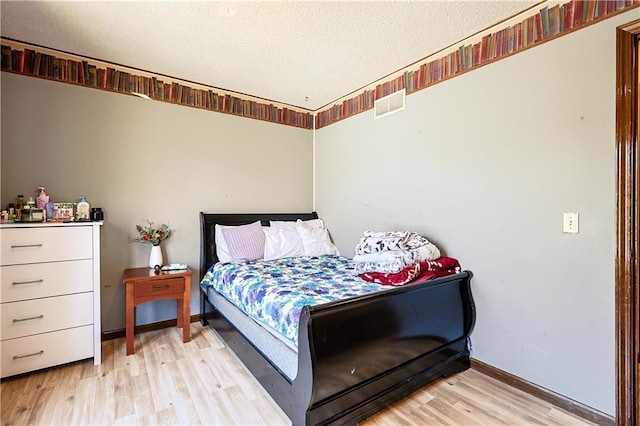 bedroom with baseboards, light wood-style floors, visible vents, and a textured ceiling