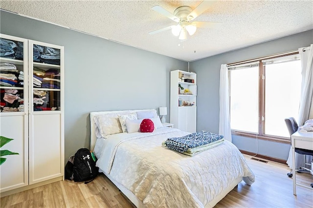 bedroom with visible vents, a textured ceiling, a ceiling fan, and light wood finished floors