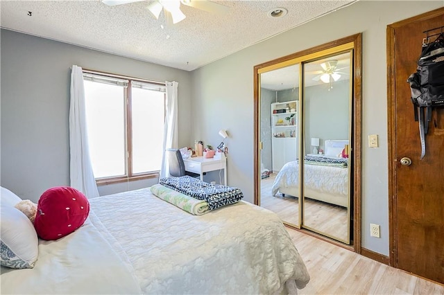 bedroom featuring a textured ceiling, a closet, light wood finished floors, baseboards, and ceiling fan