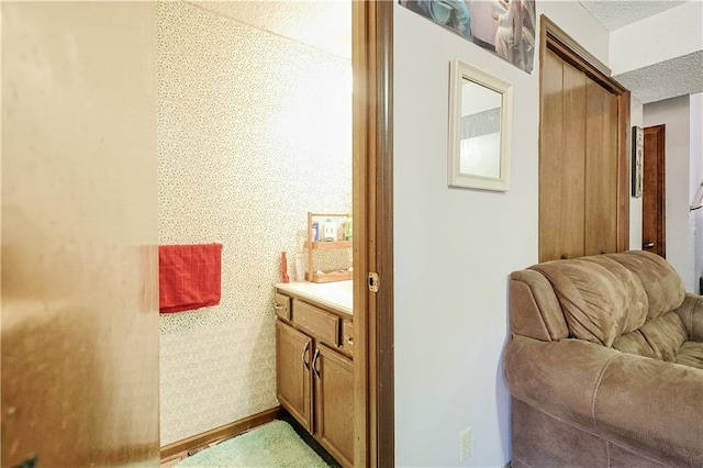 bathroom featuring wallpapered walls, vanity, baseboards, and a textured ceiling