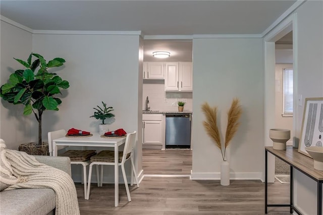 kitchen with light wood finished floors, tasteful backsplash, crown molding, white cabinetry, and stainless steel dishwasher