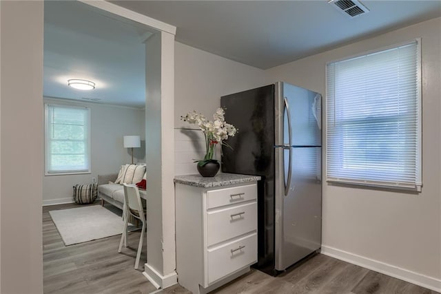 kitchen with visible vents, freestanding refrigerator, white cabinetry, wood finished floors, and baseboards