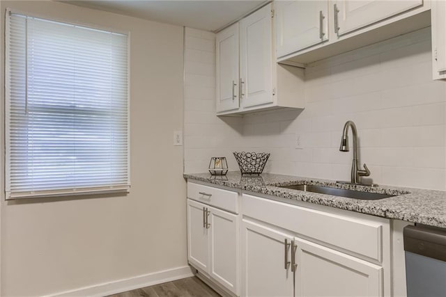 kitchen featuring wood finished floors, a sink, white cabinets, light stone countertops, and dishwasher