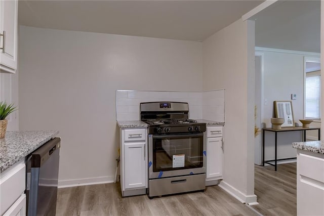 kitchen featuring appliances with stainless steel finishes, white cabinets, light wood-style flooring, and light stone counters