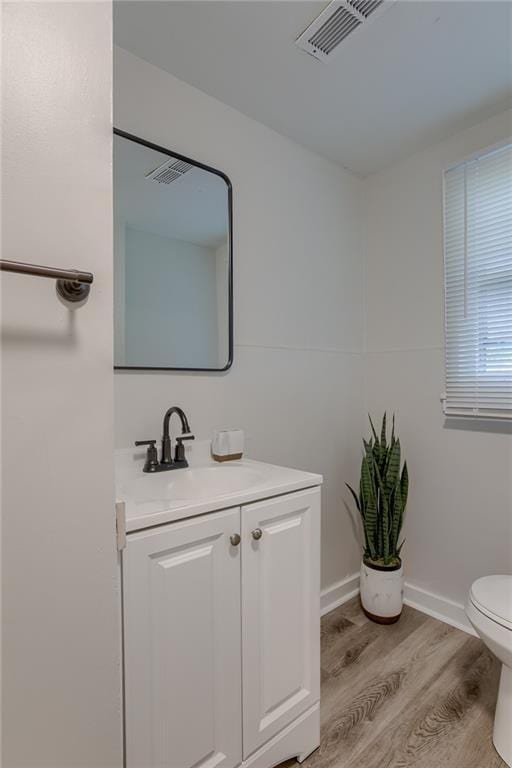 bathroom featuring baseboards, visible vents, toilet, wood finished floors, and vanity