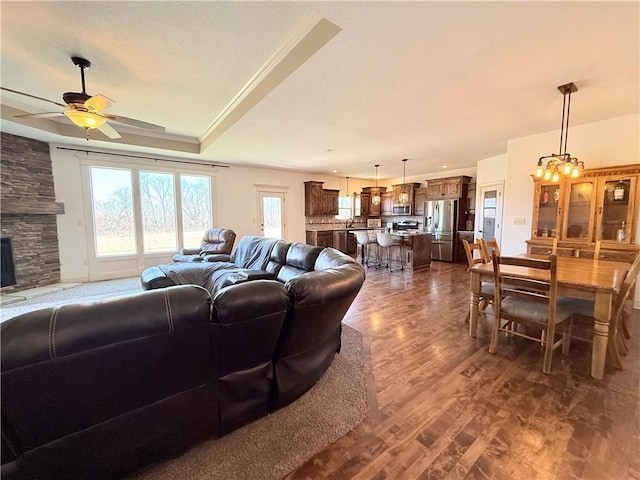 living area featuring ornamental molding, a ceiling fan, a textured ceiling, dark wood-style floors, and a raised ceiling