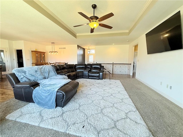 living room featuring a ceiling fan, baseboards, ornamental molding, a raised ceiling, and carpet flooring