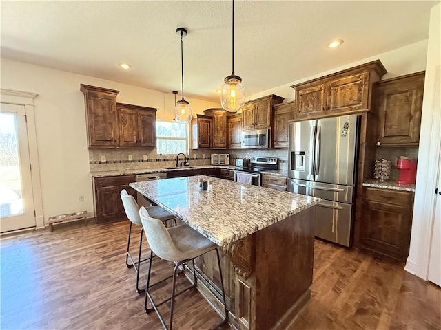 kitchen featuring light stone counters, a kitchen island, a sink, stainless steel appliances, and dark wood-type flooring