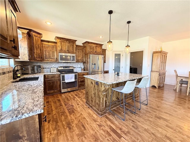 kitchen featuring wood finished floors, stainless steel appliances, decorative backsplash, and a sink