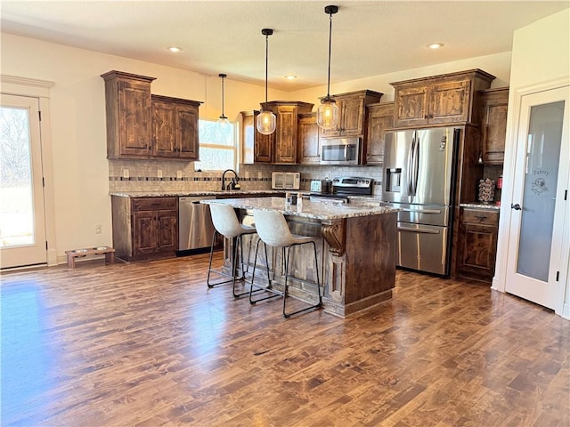 kitchen featuring backsplash, a kitchen island, light stone countertops, appliances with stainless steel finishes, and dark wood-style flooring