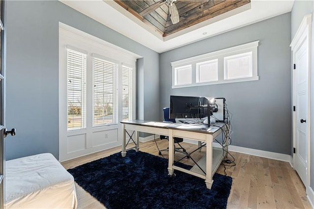 office area with a raised ceiling, baseboards, and light wood-type flooring