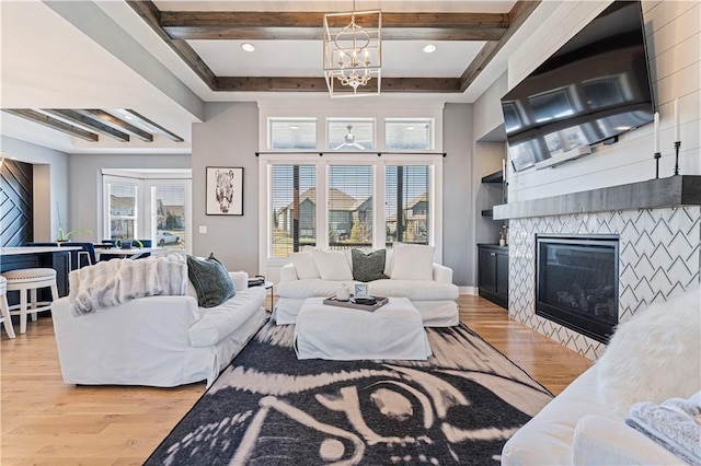 living room with a stone fireplace, beam ceiling, light wood-style floors, and an inviting chandelier