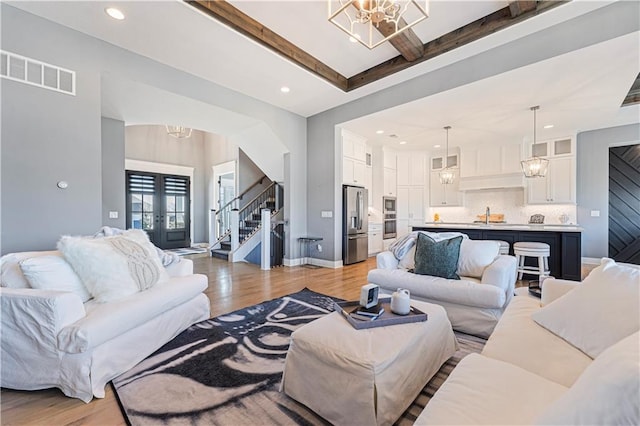 living room with visible vents, light wood-type flooring, stairs, and an inviting chandelier