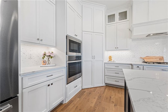 kitchen with light wood-type flooring, appliances with stainless steel finishes, white cabinets, and decorative backsplash