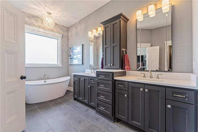 full bath with double vanity, a freestanding tub, a notable chandelier, and a sink