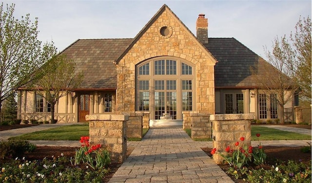 view of front of home featuring stone siding, french doors, a chimney, and roof with shingles