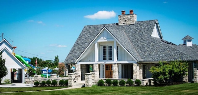 exterior space featuring stone siding, board and batten siding, a chimney, and a front lawn