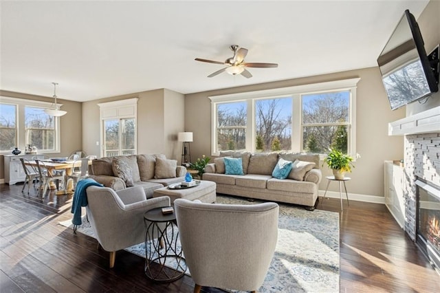 living area featuring a fireplace, dark wood-style flooring, a wealth of natural light, and ceiling fan