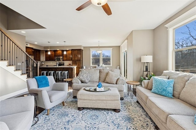 living area with stairway, baseboards, and ceiling fan