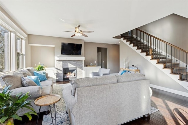 living room with dark wood-style floors, a fireplace, baseboards, ceiling fan, and stairs