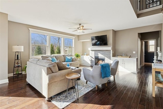 living room with a stone fireplace, baseboards, ceiling fan, and wood finished floors