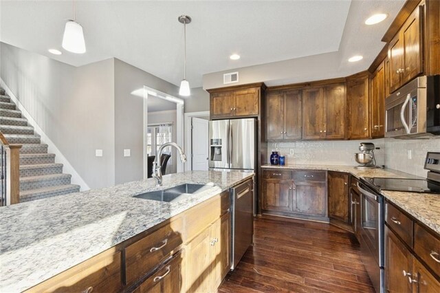 kitchen with a sink, hanging light fixtures, dark wood-type flooring, appliances with stainless steel finishes, and tasteful backsplash