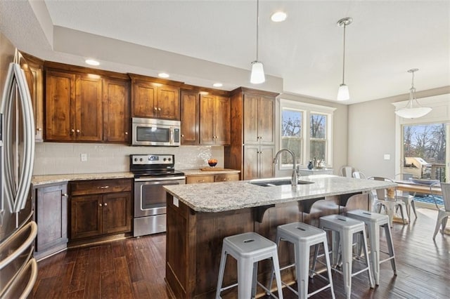 kitchen featuring dark wood finished floors, a sink, stainless steel appliances, a kitchen bar, and backsplash