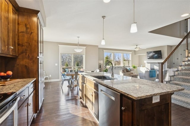 kitchen featuring a ceiling fan, a sink, appliances with stainless steel finishes, a fireplace, and light stone countertops