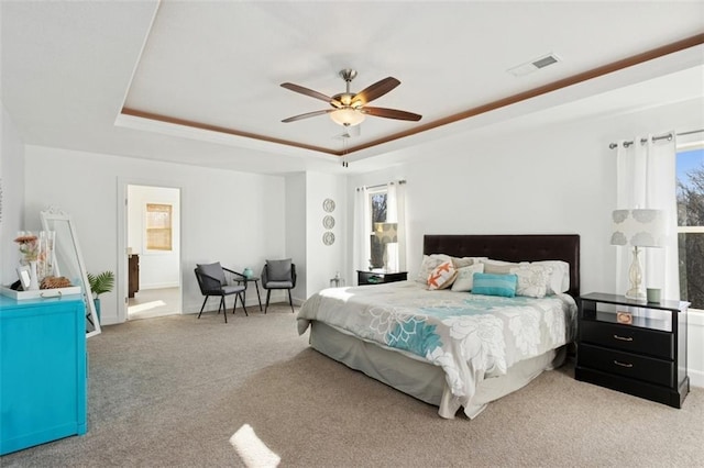 carpeted bedroom featuring visible vents, baseboards, a raised ceiling, and a ceiling fan