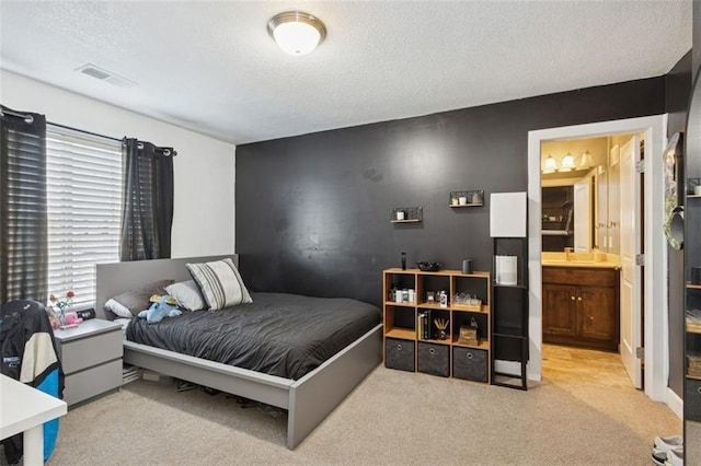 bedroom with visible vents, ensuite bathroom, a textured ceiling, and carpet flooring