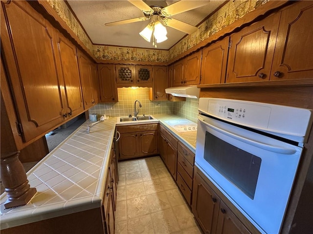 kitchen with white appliances, a sink, tile counters, and under cabinet range hood