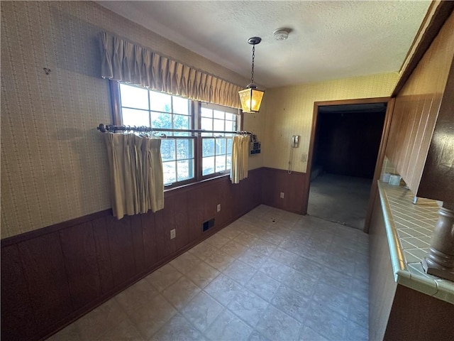 unfurnished dining area featuring light floors, visible vents, wainscoting, wood walls, and a textured ceiling