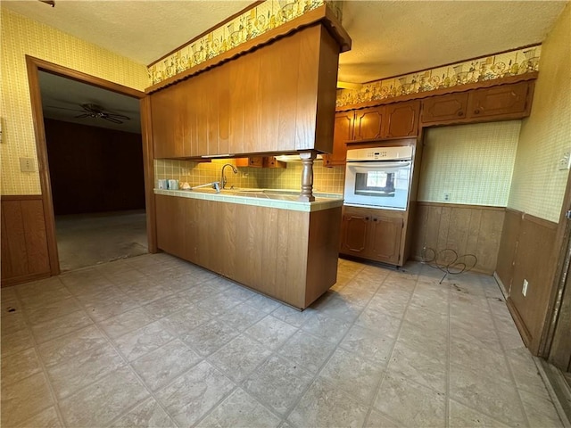 kitchen featuring oven, a wainscoted wall, tile counters, light floors, and wallpapered walls