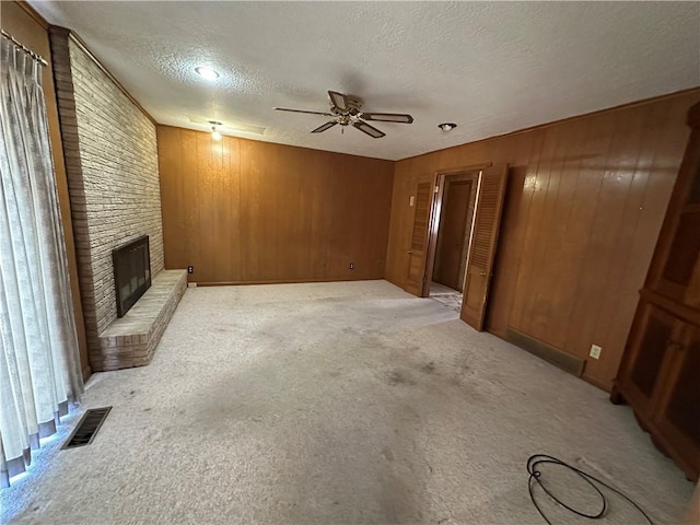 unfurnished living room with a textured ceiling, ceiling fan, light colored carpet, visible vents, and a brick fireplace