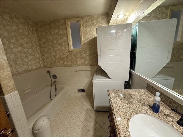 bathroom with wallpapered walls, wainscoting, stacked washer and clothes dryer, tile patterned floors, and a garden tub