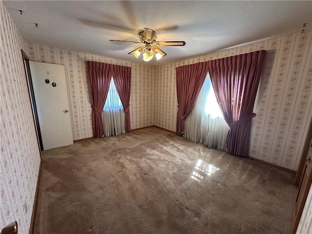 spare room with carpet floors, ceiling fan, a textured ceiling, baseboards, and wallpapered walls