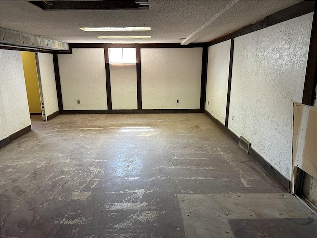 empty room with a textured wall, a textured ceiling, and unfinished concrete floors