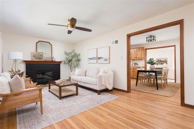 living room with a ceiling fan, baseboards, visible vents, and light wood finished floors